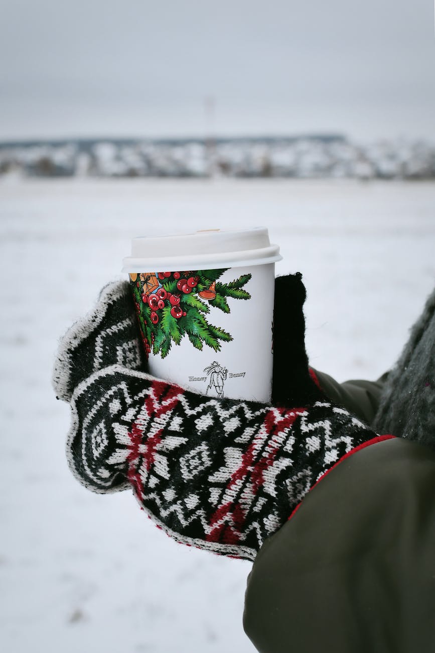 holding christmas disposable coffee cup with mittens