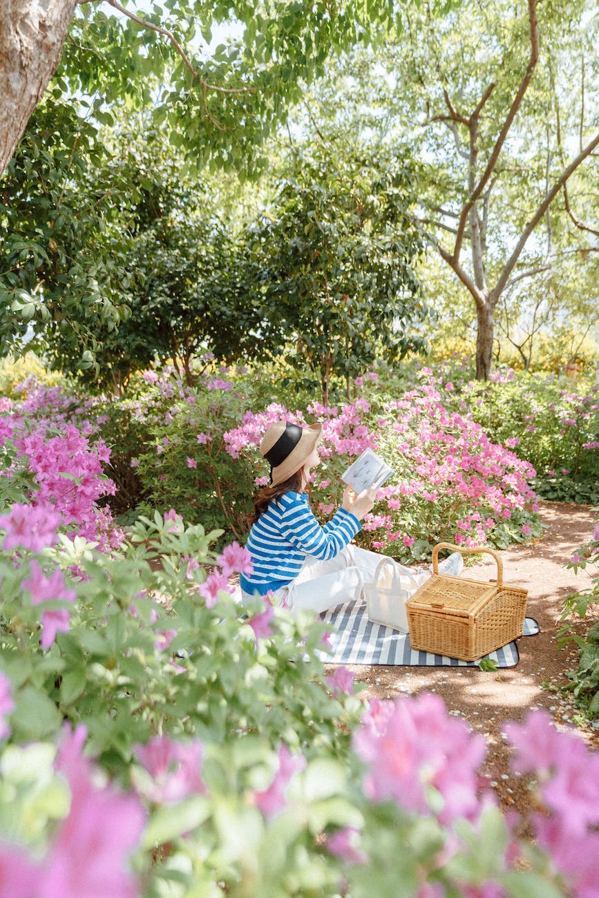 woman sitting on a blanket in a park among flowers and reading a book