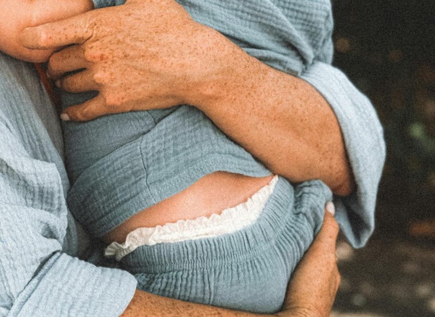 freckled hands of a woman holding a baby