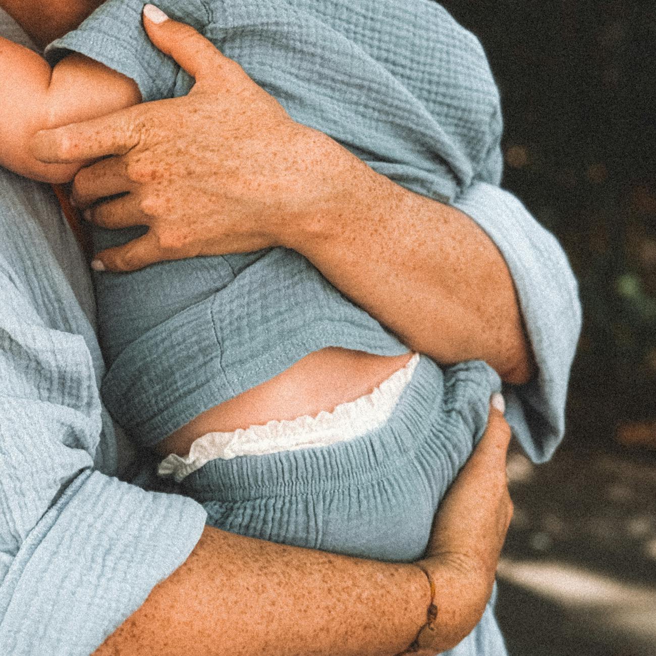 freckled hands of a woman holding a baby