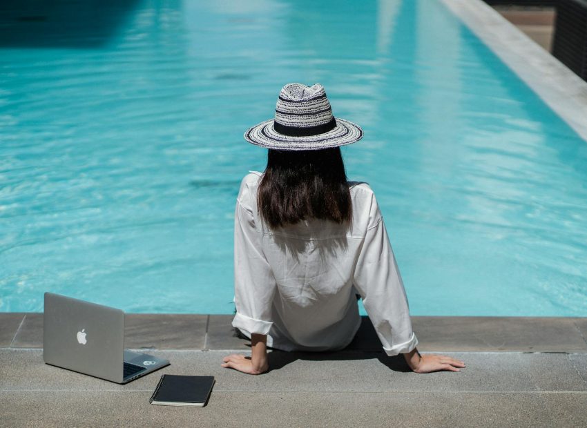 faceless female freelancer resting at poolside after work on laptop