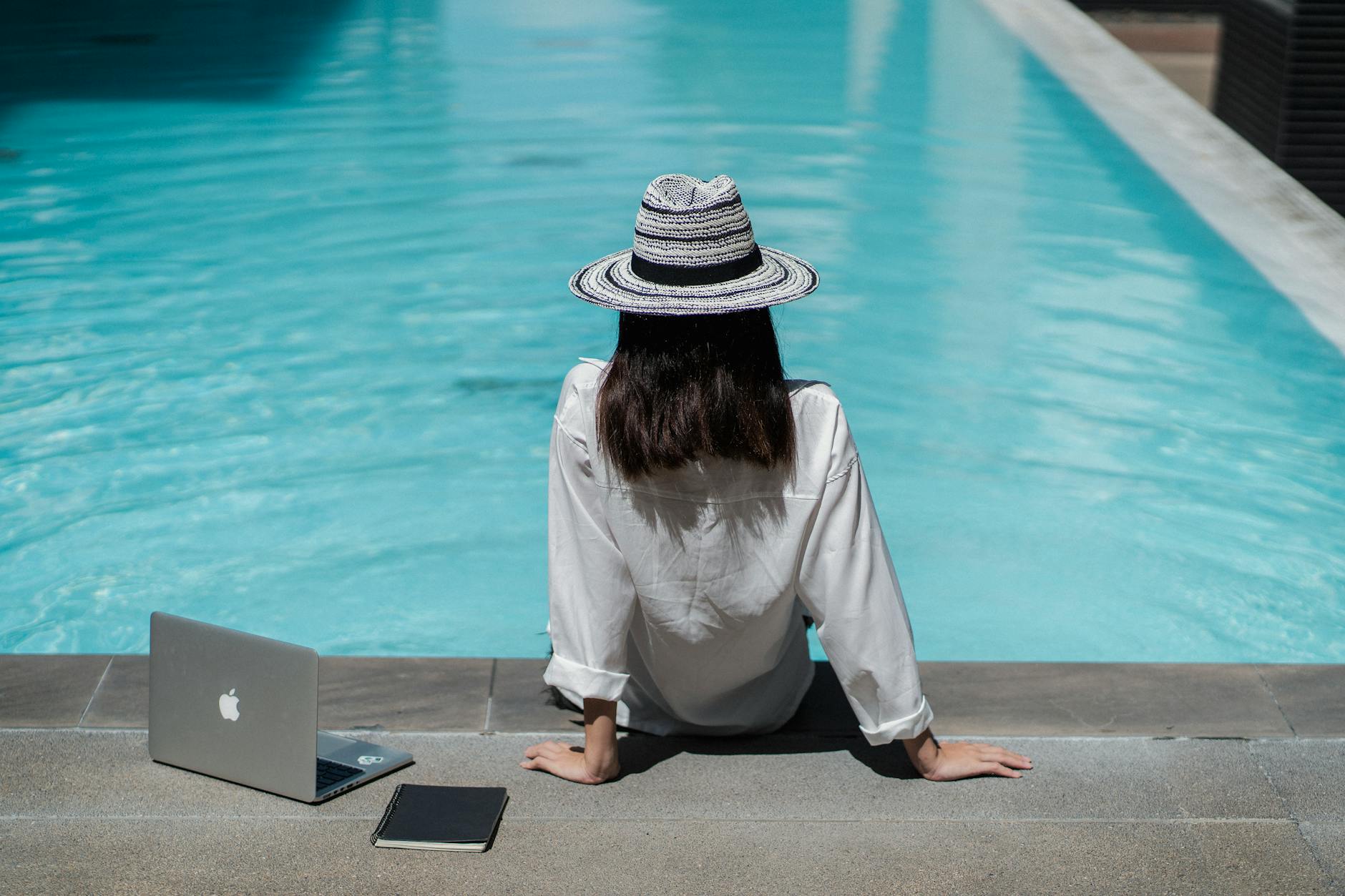 faceless female freelancer resting at poolside after work on laptop